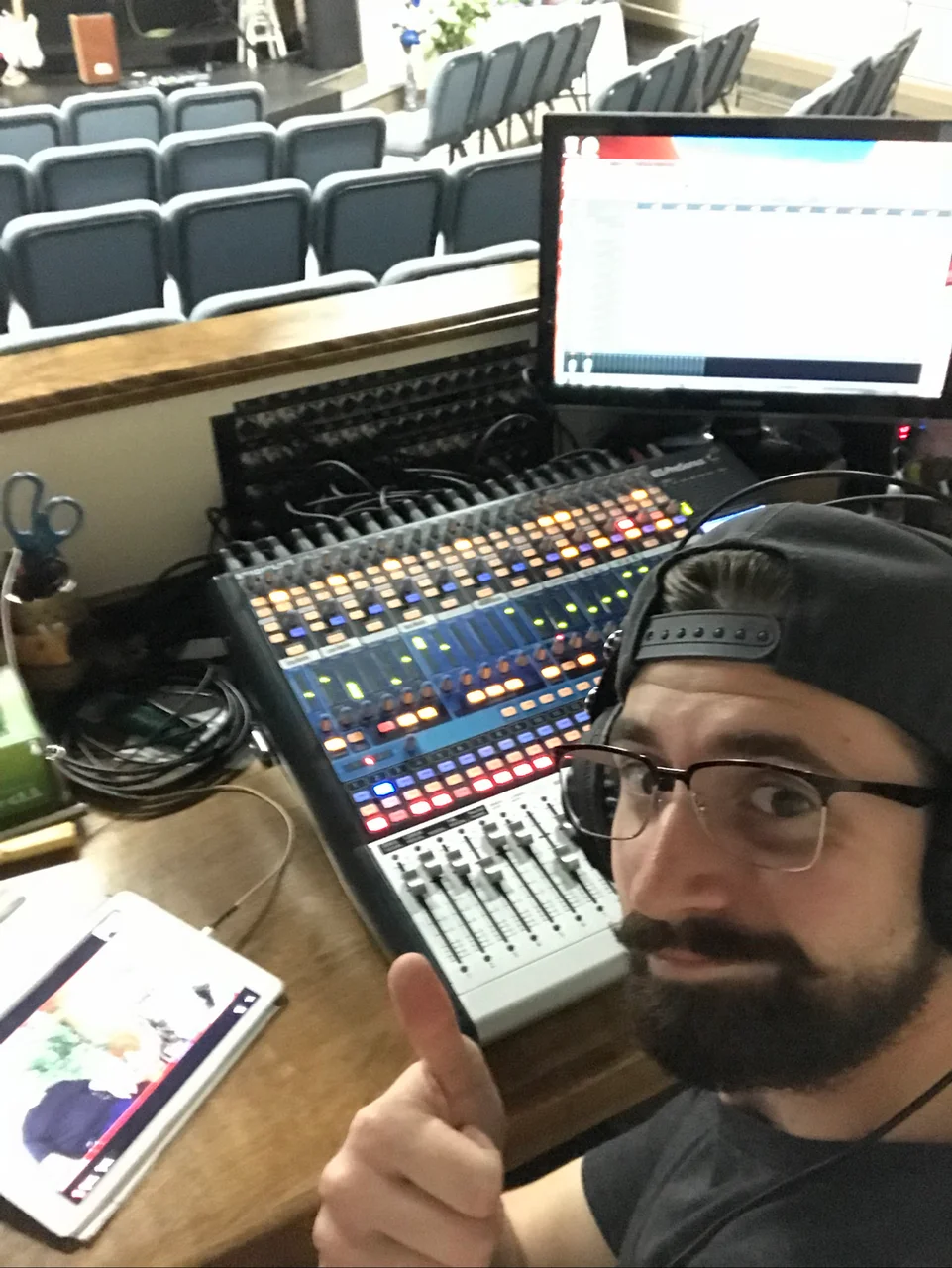 Tim taking a selfie beside an audio mixing console, with church seating behind him.