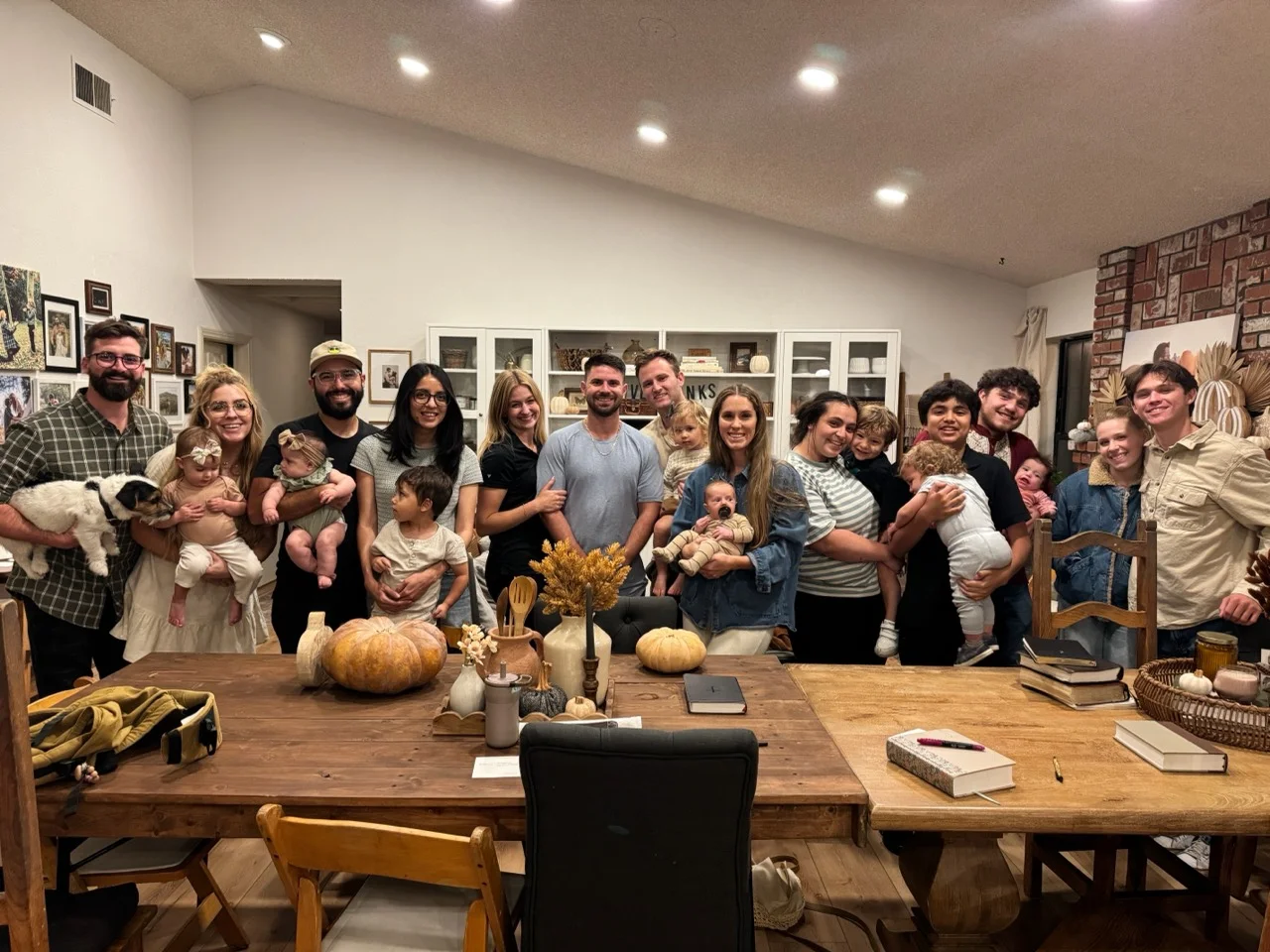 Adults and children gathered behind a dining table with books, notebooks, and autumn decorations.